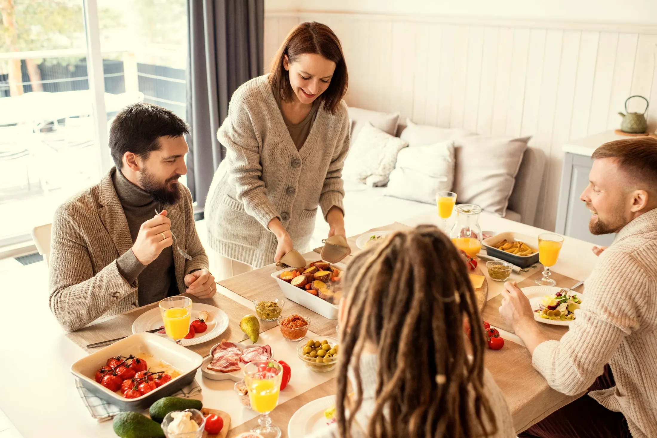 Friends reaching across a bright table of shared brunch dishes and orange juice
