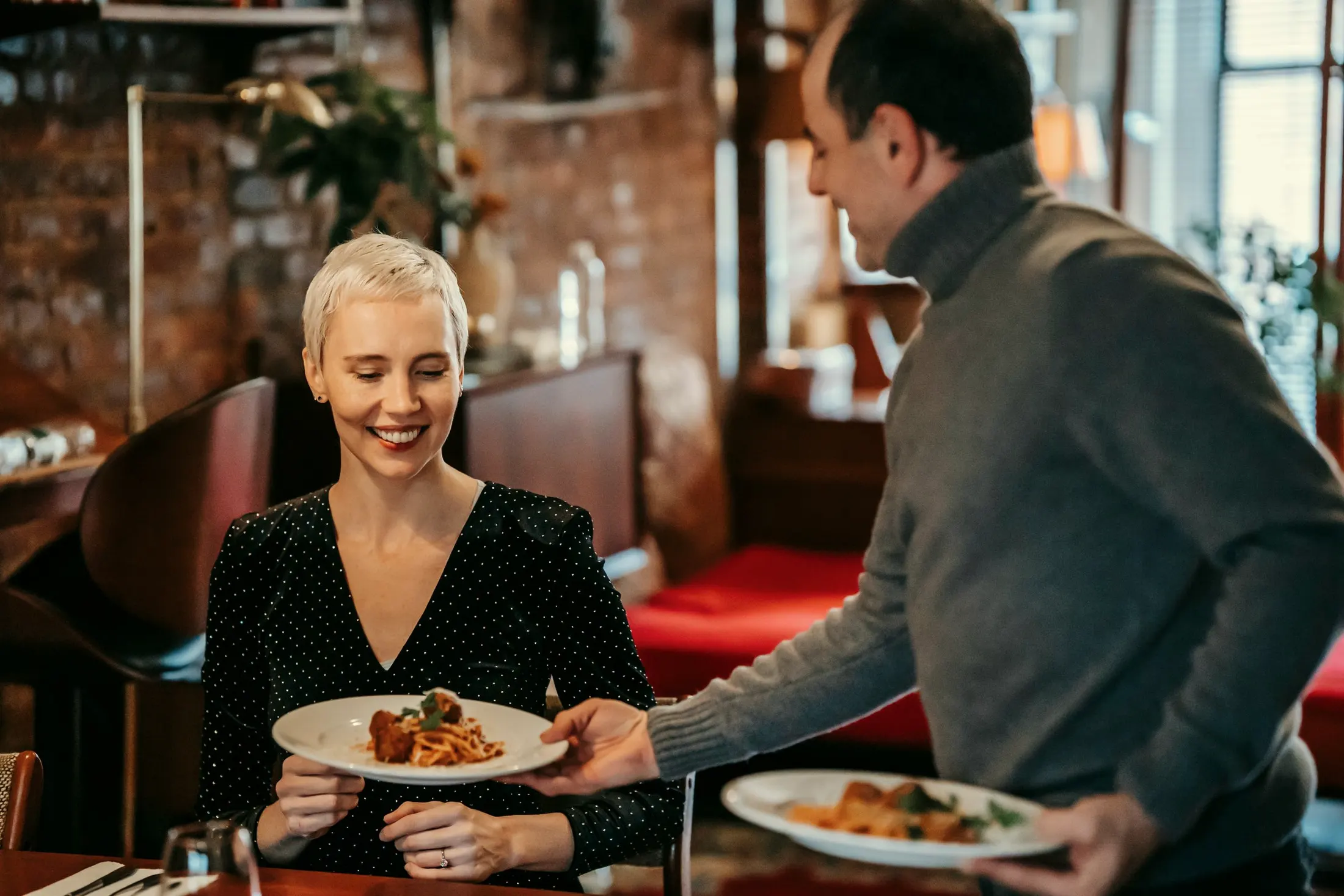 A smiling couple sharing plates of pasta at a restaurant table
