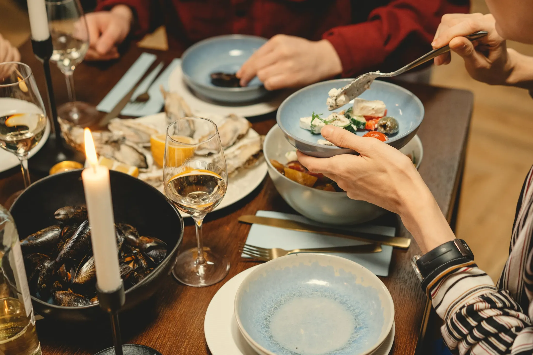 Hands reaching across a candlelit table for shared plates, mussels and wine